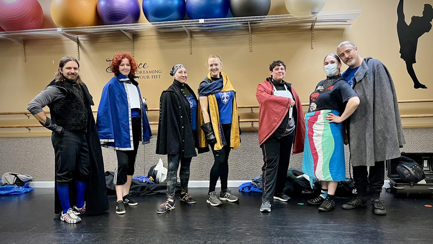 Boston Academie d'Armes rapier class during Cloaktober. Each fencer is wearing a fancy fencing cloak except Bella who is wearing a beach towel around their waist.