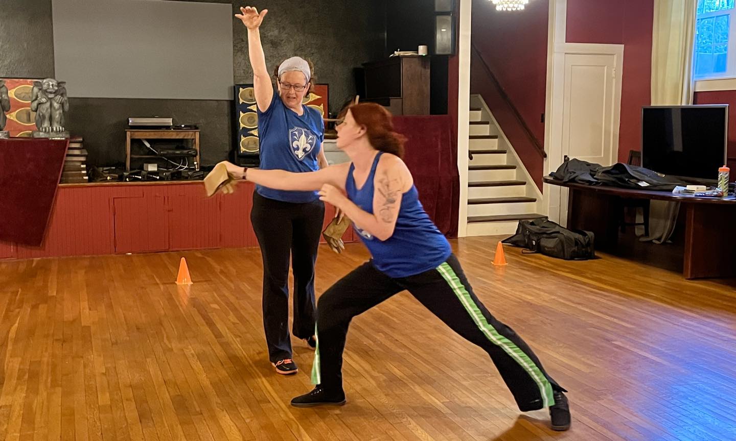 Two women historical fencers in Boston work on their lunge with a warm-up game.