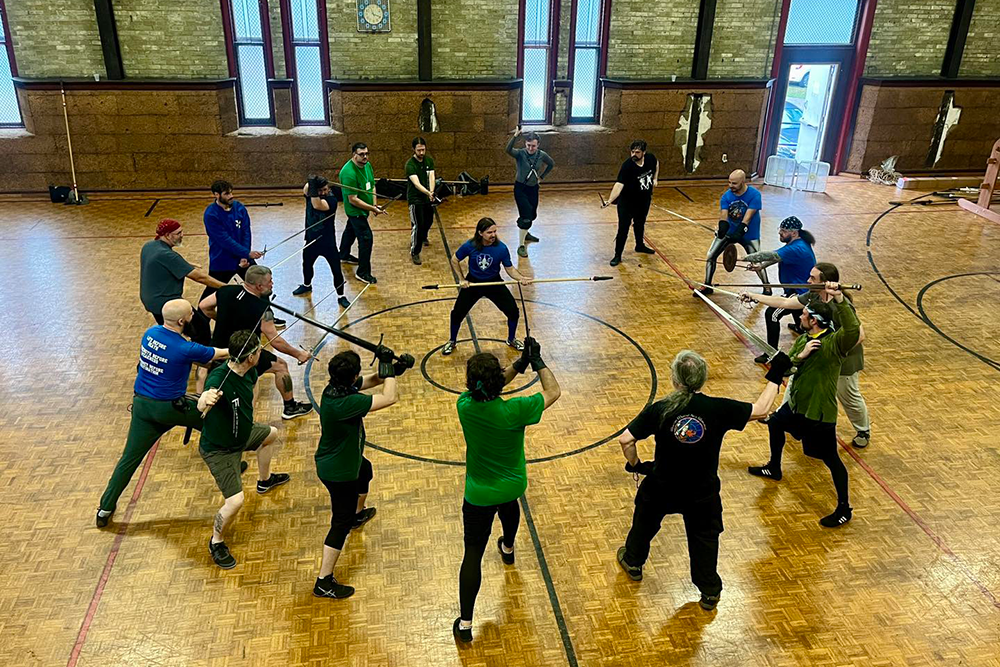 Justin surrounded by historical fencers with swords at WMAW 2024 at his jaegerstock workshop